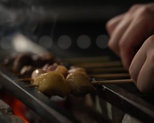 炭火で焼鳥を焼く職人の手元。『Sleep. Beauty. Fire. 焼鳥さいとう』のイメージ